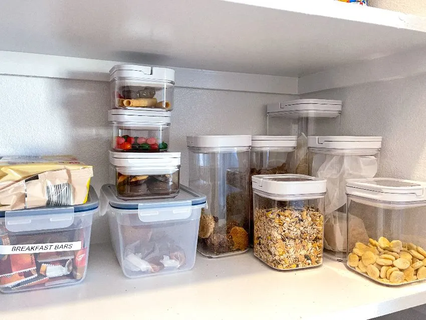 Deep pantry organization with various types of cookies, cereal and snacks tidily put in plastic containers