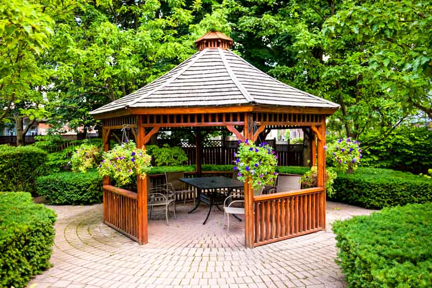Outdoor area with gazebo, table, chairs, hedge plants, and trees