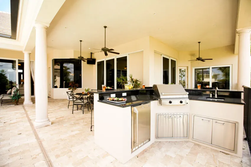 Outdoor kitchen with granite countertop, sink, faucet, tile flooring, ceiling fan, table, and chairs