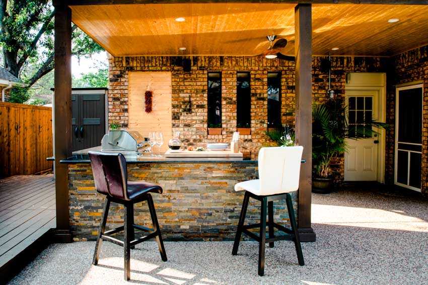 Outdoor kitchen with stone veneer, high chairs, countertops, wood deck, and ceiling lights