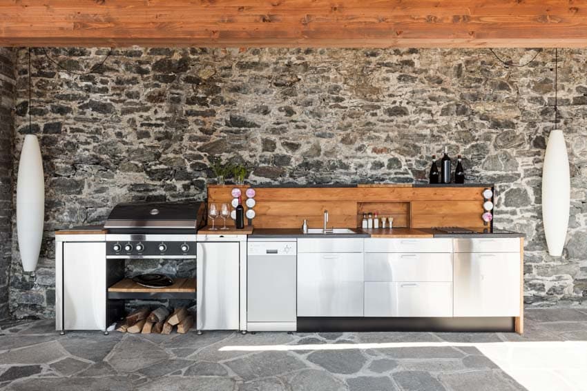 Outdoor kitchen with stone wall, countertop, built in cutting board, wood backsplash, metal cabinets, and stove