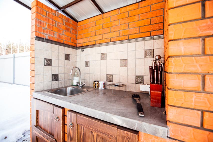 Outdoor kitchen with tile backsplash, epoxy countertop, sink, and faucet