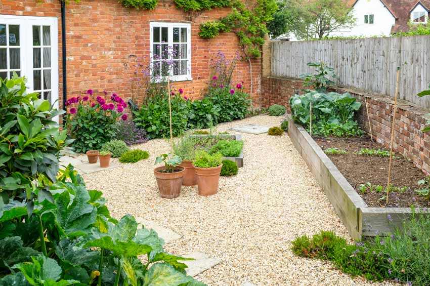 Outdoor patio with gravel surface, plants, flowers, and raised garden bed