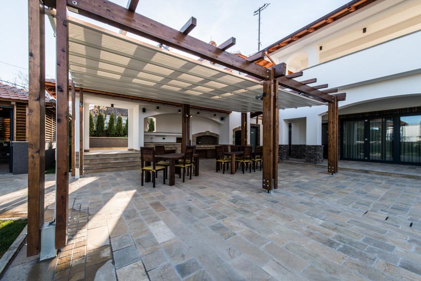 Outdoor patio with pergola, stone tile flooring, table, chairs, and roof shade