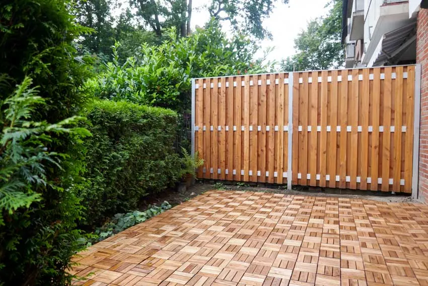Patio with wood tile surface, plants, and board on board fence