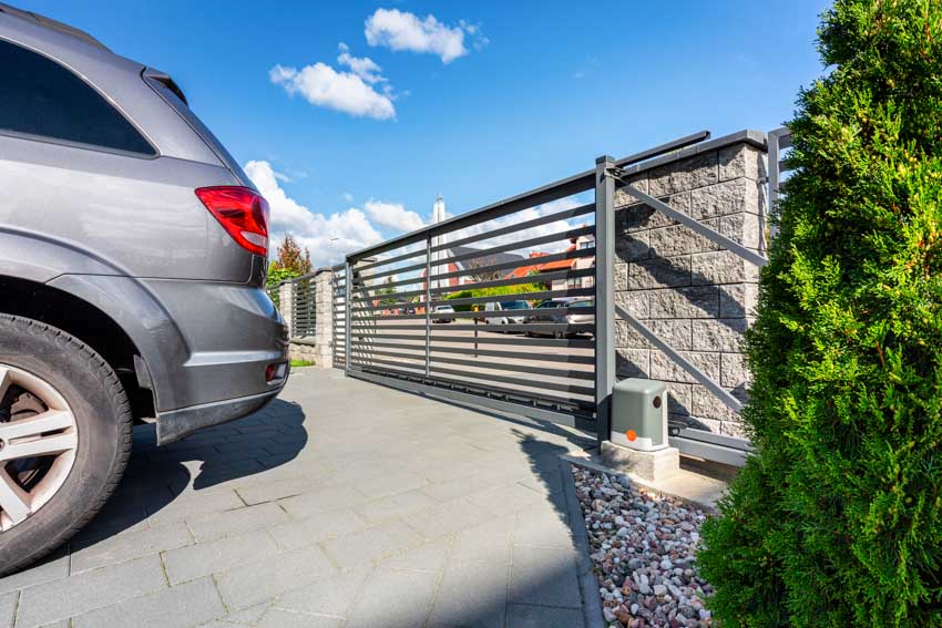 Residential driveway with cantilever sliding gate, car, and hedge plants
