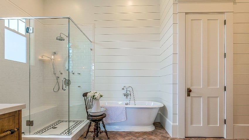 A rustic feel farmhouse style bathroom with full horizontal shiplap walls, large glass shower and antique look freestanding bathtub