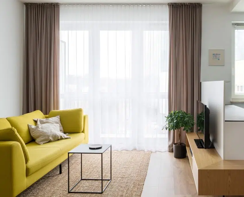 Scandinavian designed and colorful living room with big window behind decorative layered curtains, yellow sofa and tv