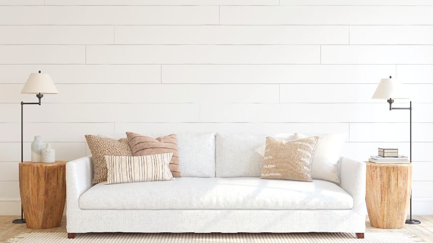 Room with horizontal shiplap walls, white sofa, wooden side tables and floor lamps