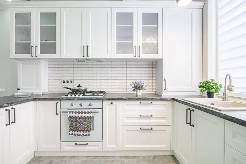 A simple white designed kitchen with linoleum countertops, gas stove and potted plants accents