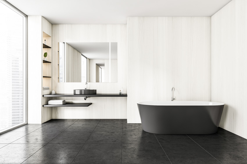 Black and white bathroom with tub, textured floor, floating single sink vanity, mirror, shelves, and window