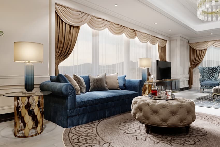 Spacious room with blue sofa in front of the window with draping curtains and a soft quilted coffee table with decor 