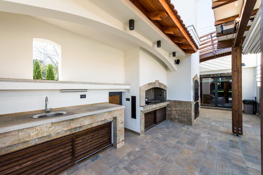 Stone outdoor kitchen with sink, countertop, built in shelf, and fireplace