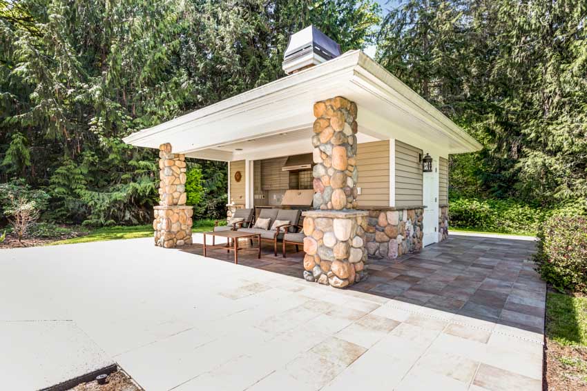 Stone outdoor kitchen with table, chairs, pillars, flat roof, and tile deck