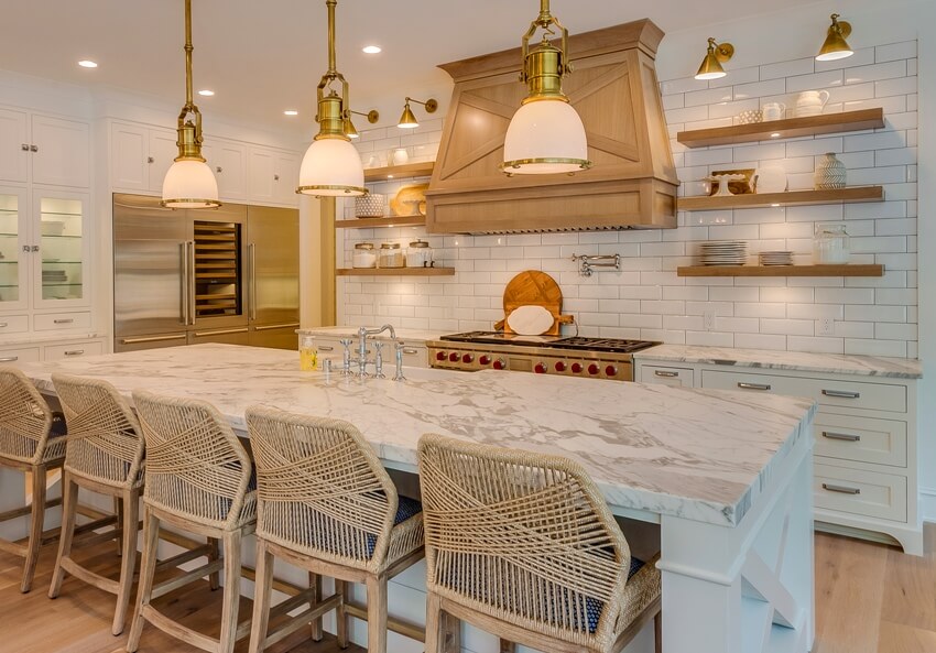 Stunning farmhouse kitchen with marble countertops, island with rattan chairs, copper wall sconces and wooden accents