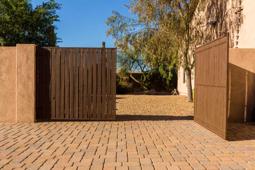 Swing gate made of vertical wood planks for residential properties with brick paver driveway
