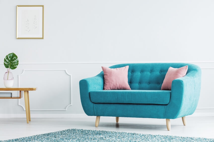 A turquoise sofa with pink cushion and white walls in a minimalist room