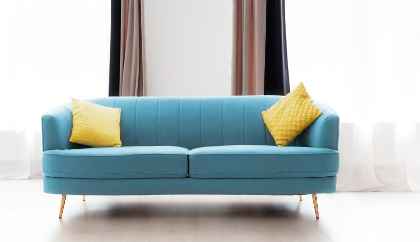 A turquoise sofa with yellow cushion with brown, black and sheer curtains behind