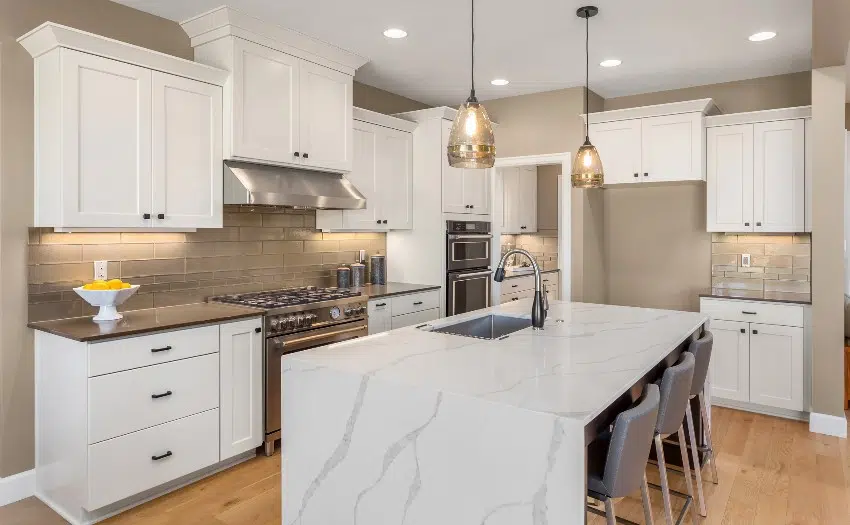 White kitchen with wood accents, waterfall marble island with sink, pendant lights and frosted glass subway tile backsplash
