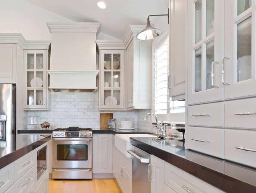 White kitchen with wooden floors, granite countertops, stainless steel appliances and wall sconce