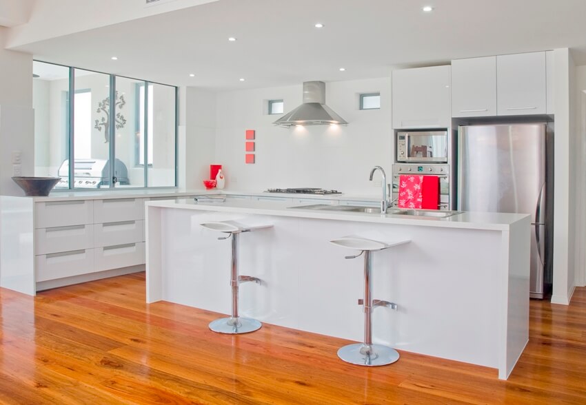 White kitchen without backsplash with stainless steel appliances and wooden floors