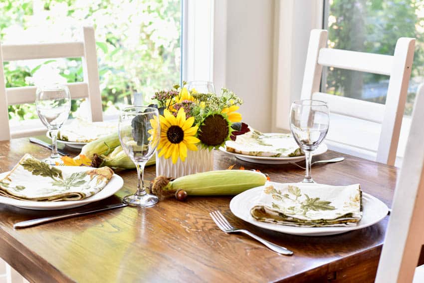 Wood dining table with plates, glasses, chairs, and flower centerpiece