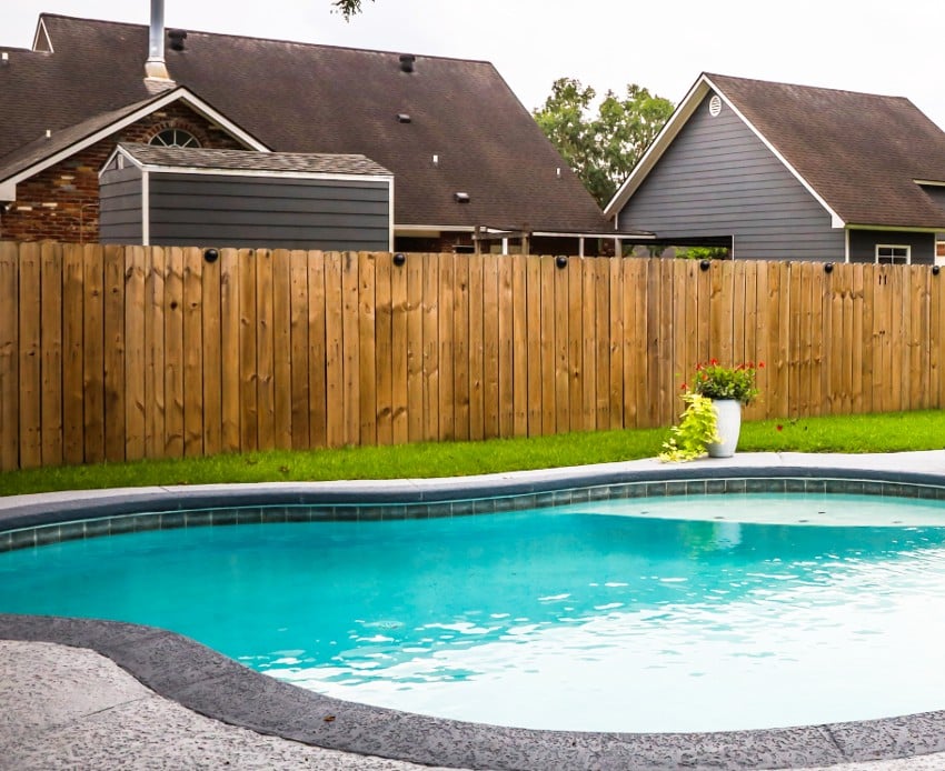 A large free form gray grey accent swimming pool in a backyard with Douglas fir fence