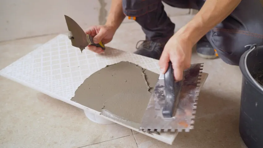 A worker applying glue to the a large format tile using a trowel