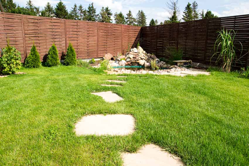 Backyard area with horizontal fence, walkway, landscaping fixtures, and hedge plants