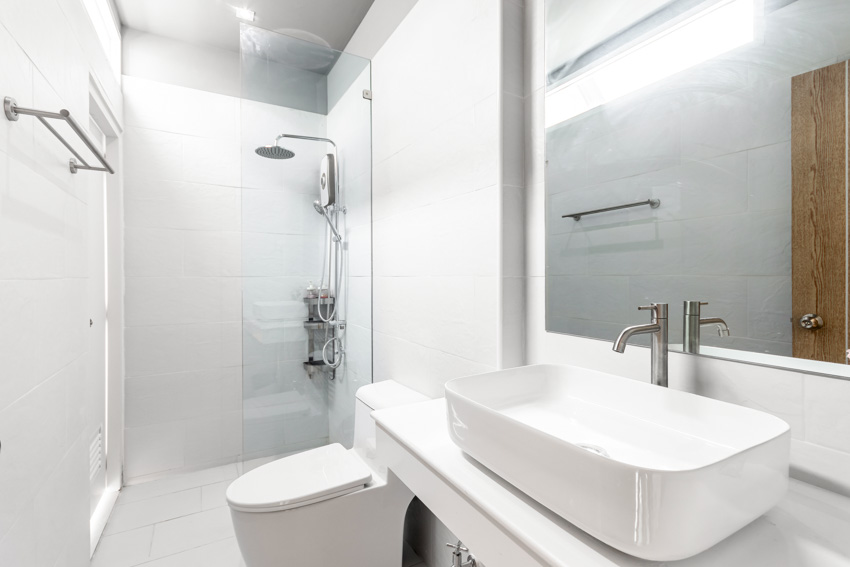 Bathroom with ceramic shower wall, glass divider, countertop, sink, mirror, toilet, and towel holder