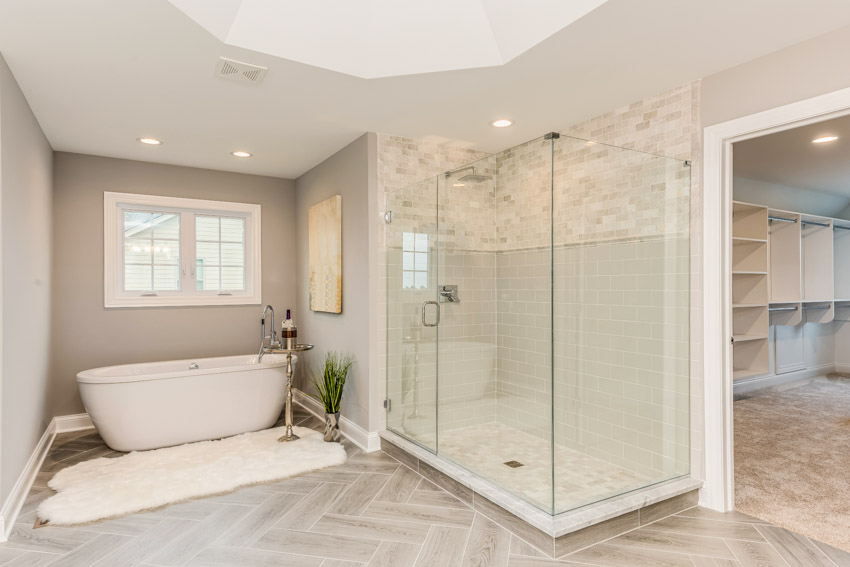 Bathroom with glass enclosure, shower wall, tub, herringbone pattern floor, and window