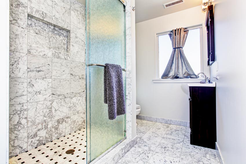 Bathroom with granite shower tile wall, glass door, towel holder, window, and curtain
