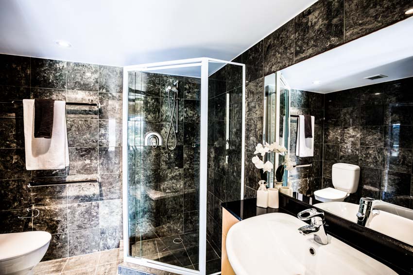 Bathroom with granite shower wall, glass door, mirror, sink, faucet, and towel holder