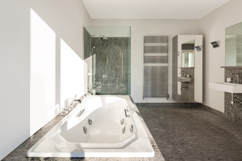 Bathroom with granite shower wall panels, tub, glass door, vanity area, mirror, and floating sink