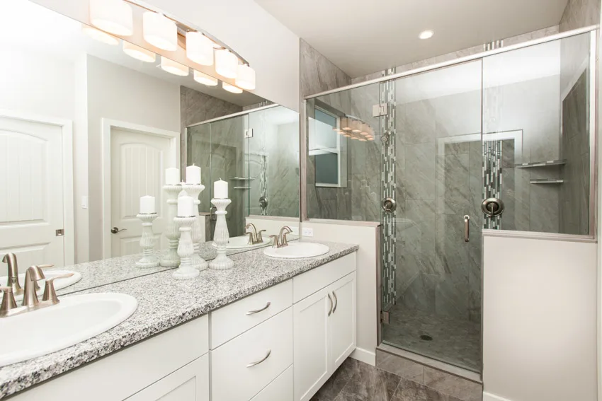 Bathroom with solid surface shower, door, countertops, drawers, sinks, and mirror