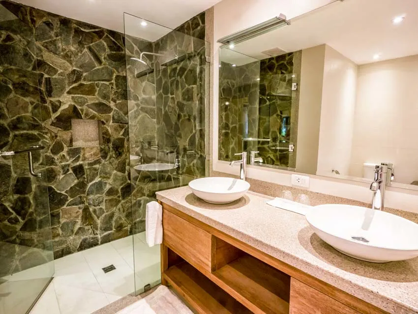 Bathroom with stone tile shower, vanity mirror, countertop, and sinks
