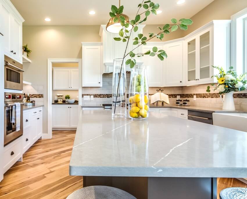 A beautiful kitchen in new luxury home with built in oven, hardwood floors and island with solid surface countertop and vased plant on top