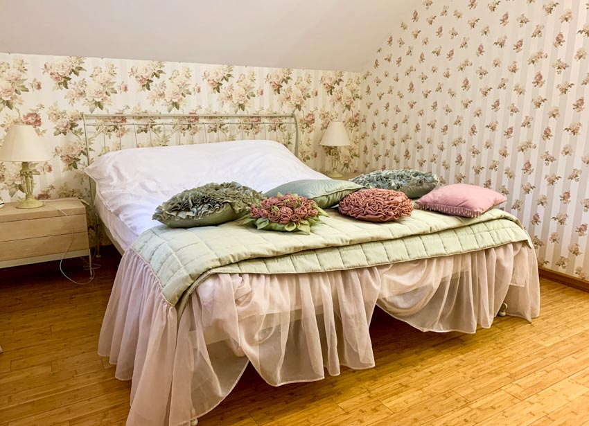 Bedroom with DIY bed skirt, wallpaper, comforter, nightstand, and wood floor