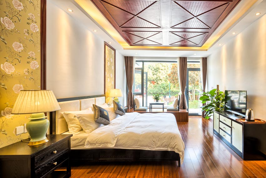 Bedroom with beadboard ceiling panels, bed, nightstand, console table, wood floor, lamp, and windows