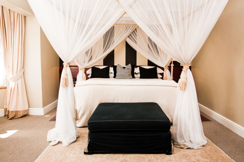 Bedroom with ceiling canopy, ottoman, pillows, rug, and window drapes