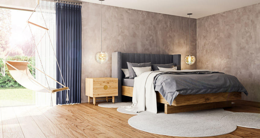 Bedroom with wood skirt frame bed, headboard, comforter, rug, pillows, nightstand, and concrete walls