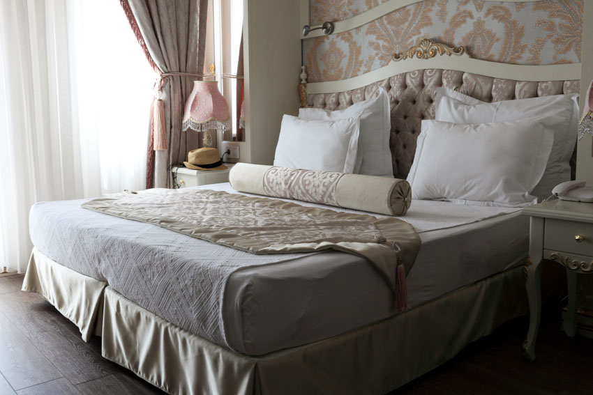 Bedroom with mattress, pillows, headboard, ornate wall, nightstands, lamp, window, and curtains