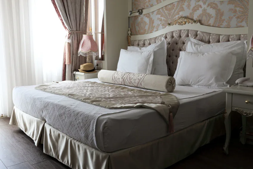 Bedroom with mattress, pillows, headboard, ornate wall, nightstands, lamp, window, and curtains