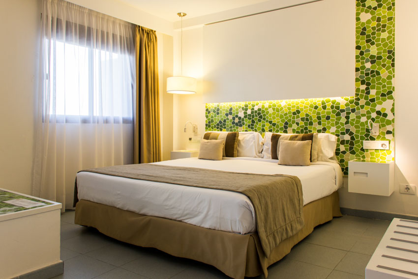 Bedroom with bed skirt, pillows, accent wall, lighting fixture, floating nightstand, and window curtains