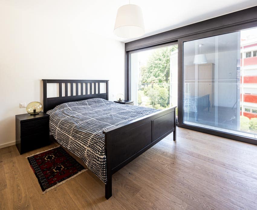 Bedroom with comforter, bed footboard, wood floor, rug, and large picture windows