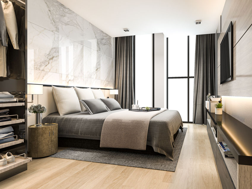 Bedroom with comforter, pillows, marble cladding wall, wood floor, rug, dark curtains and flat sheets