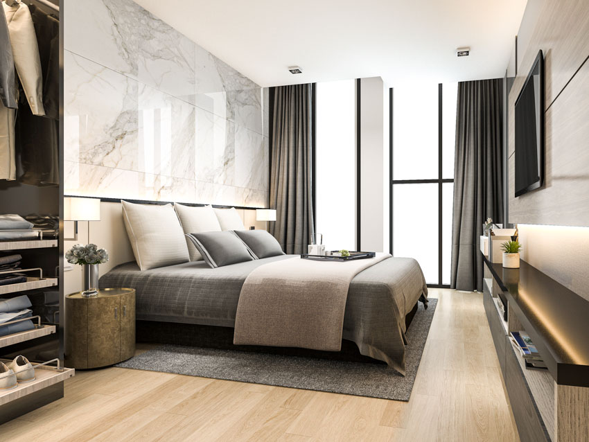 Bedroom with comforter, pillows, marble cladding wall, wood floor, rug, dark curtains and flat sheets 