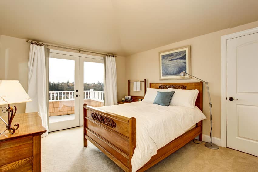 Bedroom with wood frame, bed footboard, headboard, dresser, table, lamp, windows, curtains, and white door
