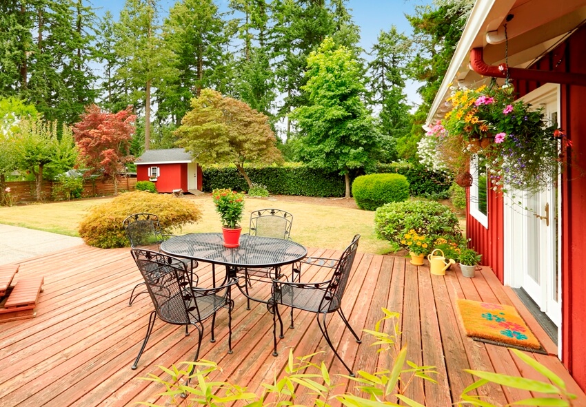 Bright red house with Douglas fir decking and patio with outdoor metal dining set and a beautiful backyard
