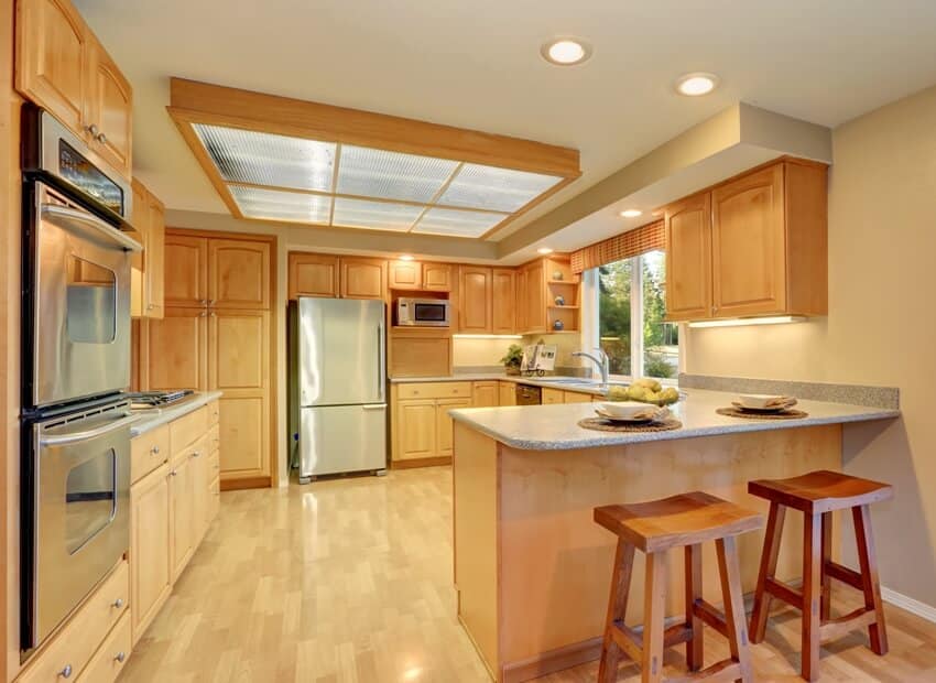 A bright wooden kitchen interior with steel appliances and fiberglass panels ceiling with lighting
